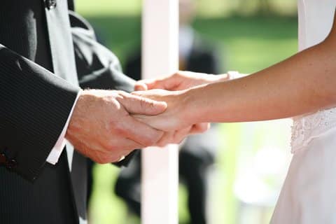 A couple holding hands at their marriage ceremony, and they are about to exchange their custom wedding vows.